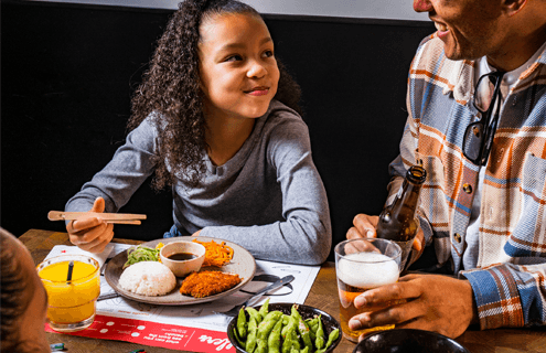 little girl glances up and her dad whilst holding mini chopsticks above a kids combo